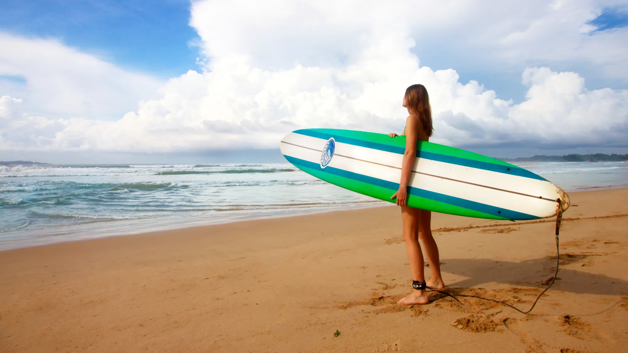 A surfer carrying a board along the beach at Weligama